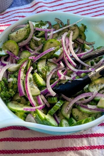 Overhead angled view of cucumber salad with parsley, red onion, and sumac.