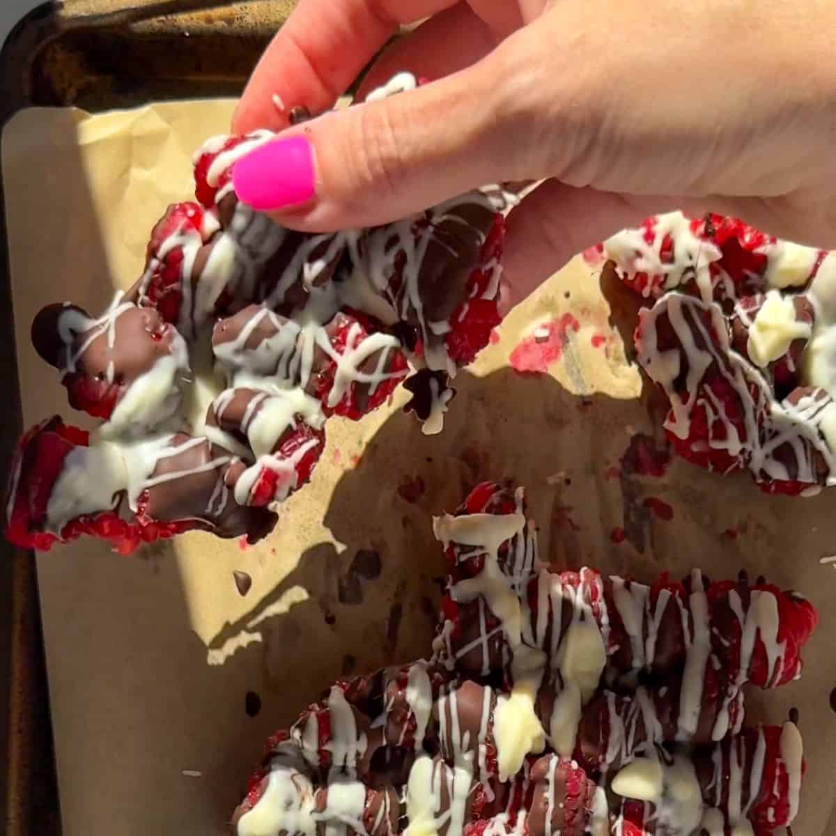 Easy white and dark chocolate raspberry bark broken into pieces on parchment paper.