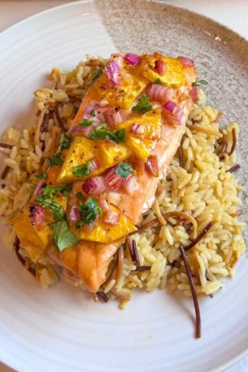 Close-up of baked salmon topped with pineapple chunks and red onion, served over rice with parsley.