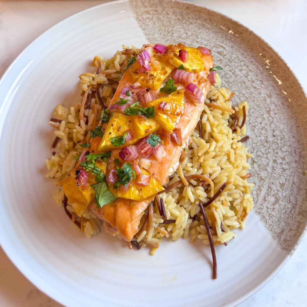 Close-up of baked salmon topped with pineapple chunks and red onion, served over rice with parsley.