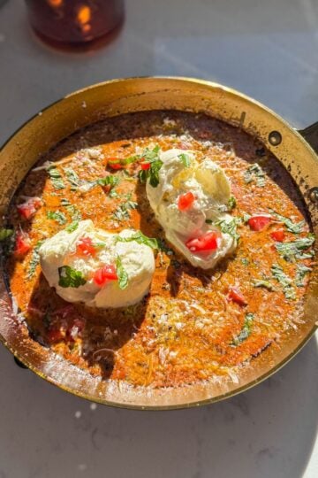 One-pan creamy pesto burrata chicken topped with tomatoes, basil, and parmesan in a skillet.