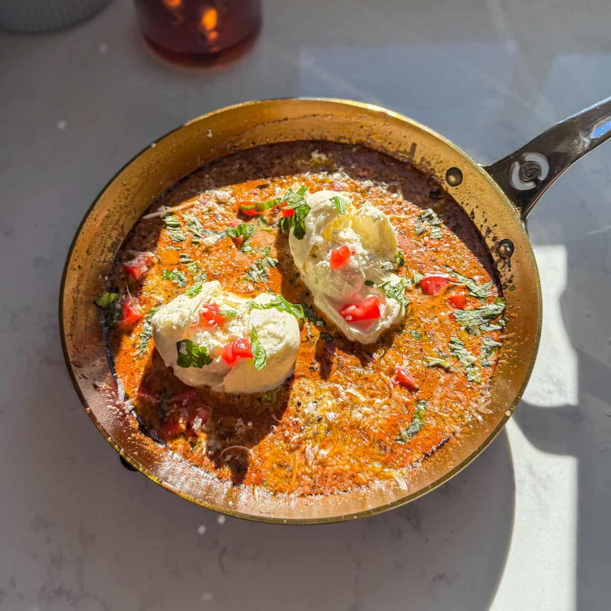 One-pan creamy pesto burrata chicken topped with tomatoes, basil, and parmesan in a skillet.