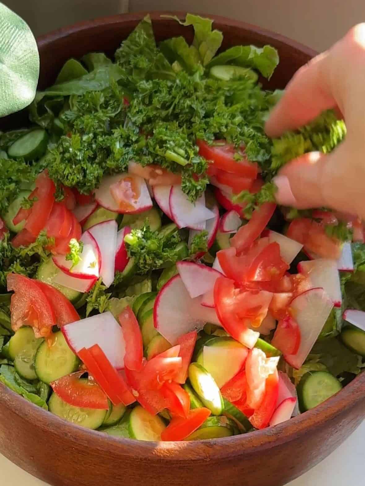 Chopped lettuce, cucumbers, tomatoes, parsley, and radishes prepared for making a fresh fattoush salad.
