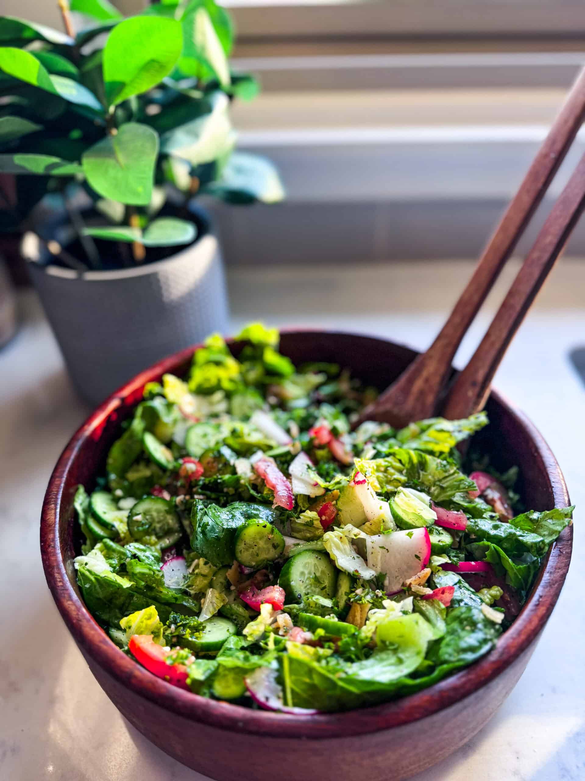 Fattoush salad in a wooden bowl with wooden salad spoons, showing crisp vegetables and toasted pita chips.
