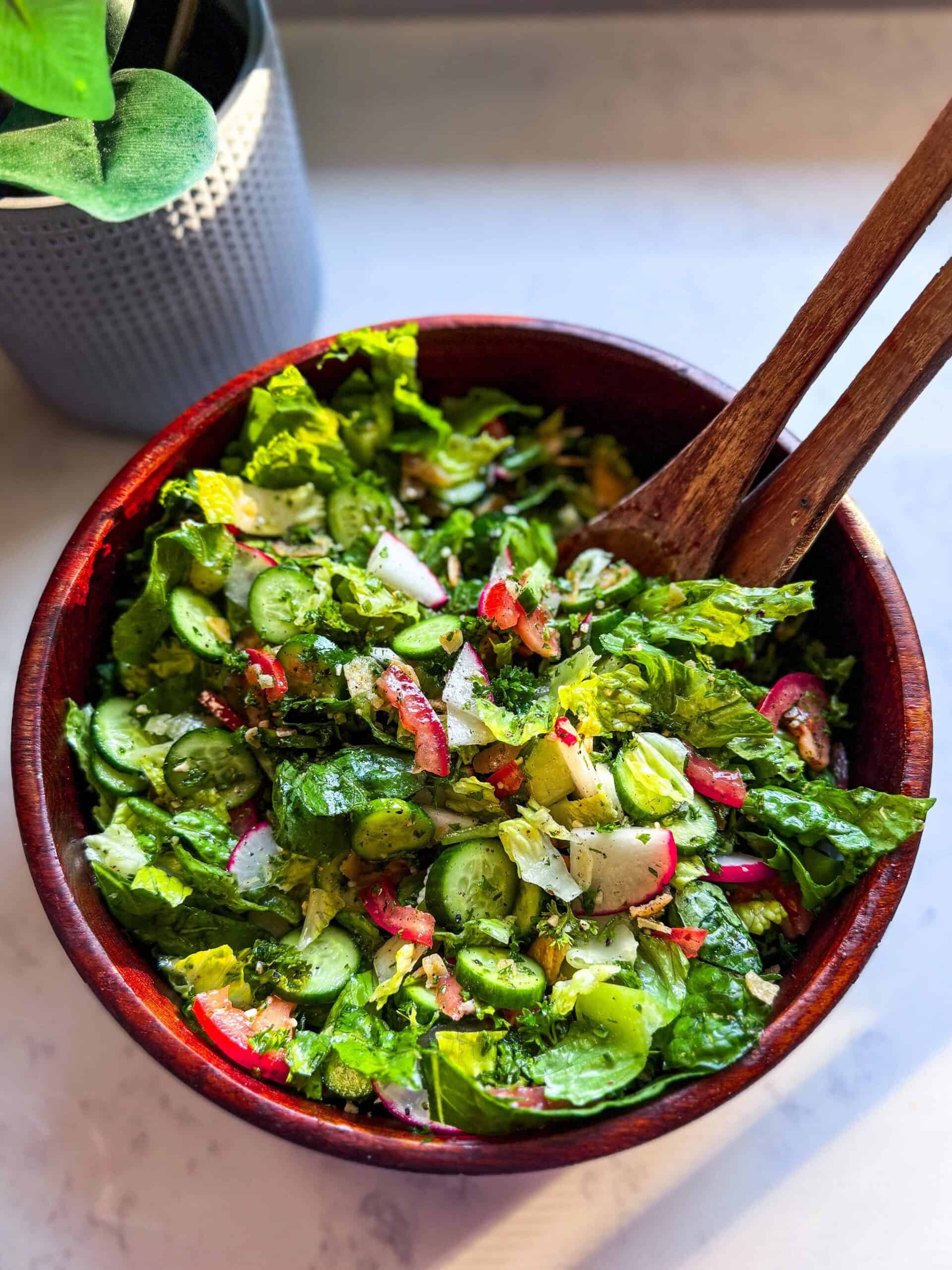 Overhead view of fattoush salad in a wooden bowl with wooden spoons, featuring fresh vegetables and sumac dressing.