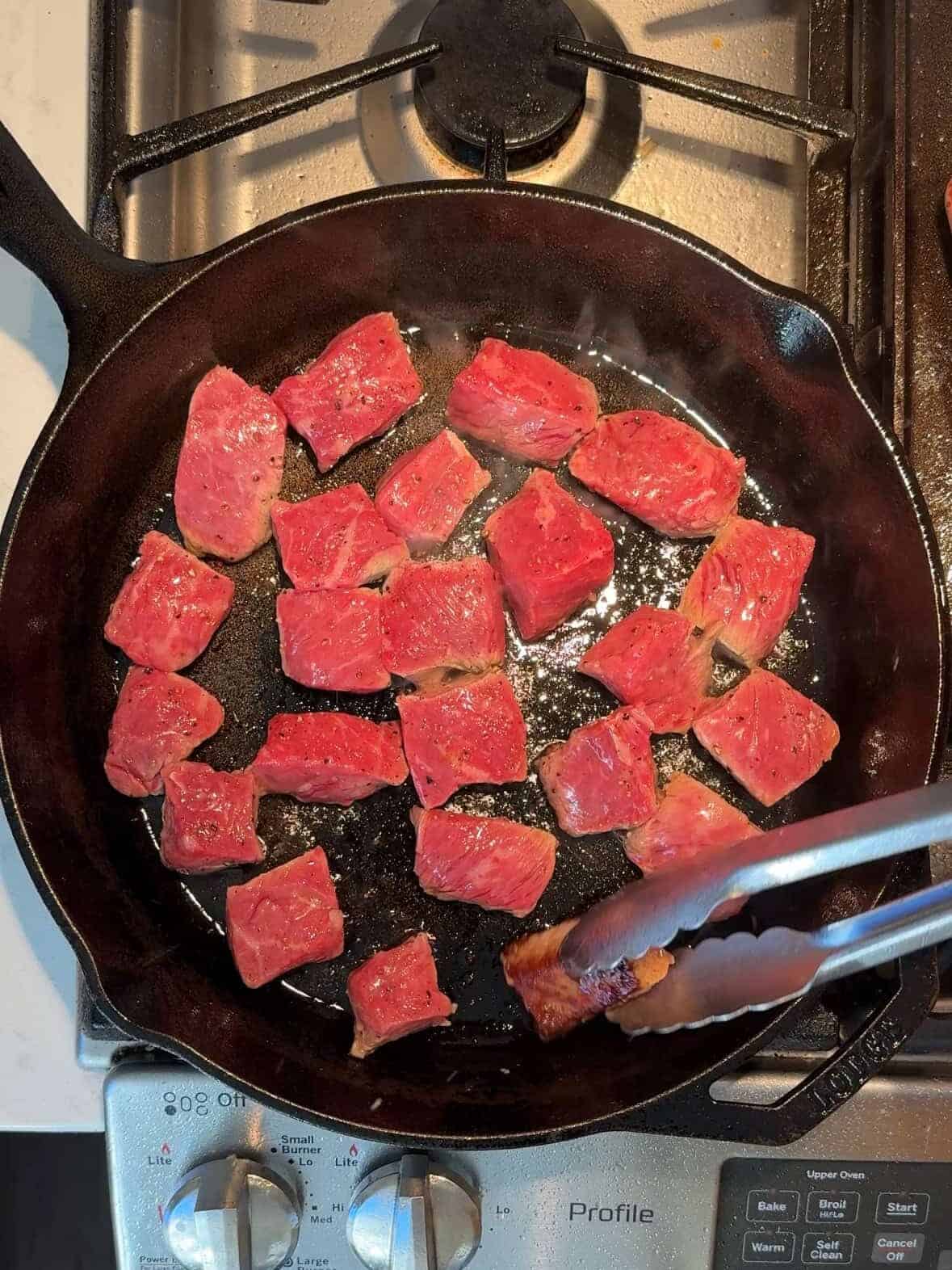 Steak bites searing in hot cast iron skillet with olive oil.