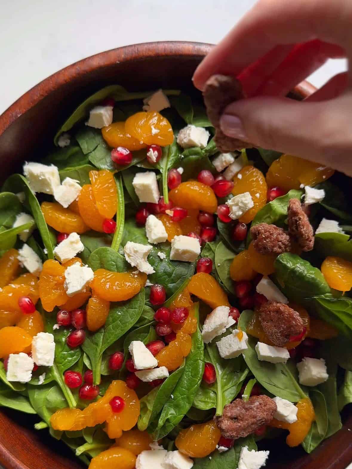 Salad ingredients arranged in a bowl before adding the pomegranate vinaigrette, including spinach, feta, oranges, and candied pecans.