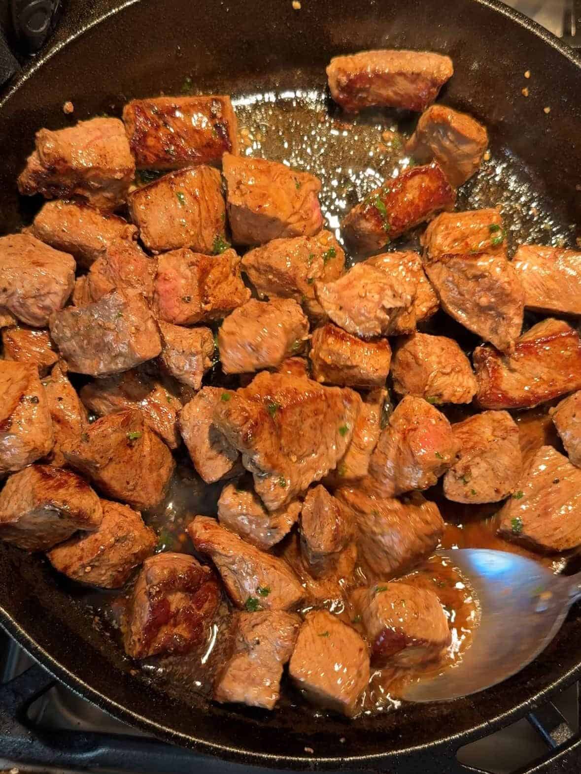 Steak bites coated in garlic butter sauce and topped with fresh parsley.