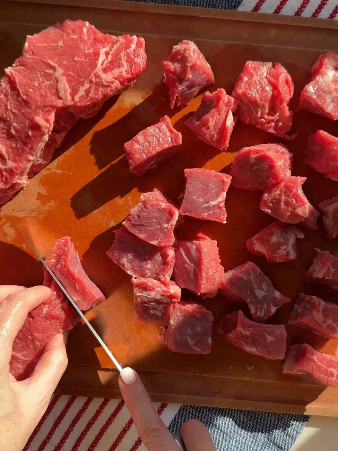 Raw New York steak cubes seasoned with salt and pepper on a cutting board.
