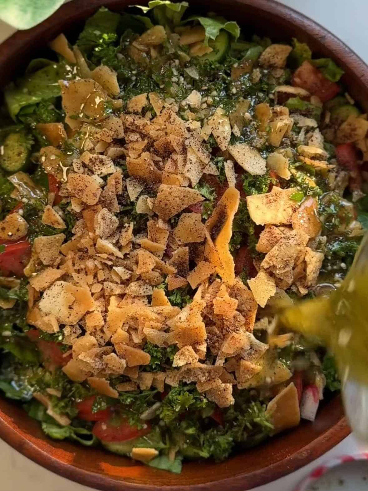 Pouring homemade fattoush salad dressing over chopped vegetables right before serving.