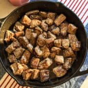 Overhead photo of garlic butter steak bites in cast iron pan on tablecloth with candle.