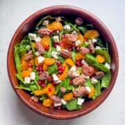 Spinach salad with pomegranate dressing ingredients displayed in a wooden bowl, photographed overhead.