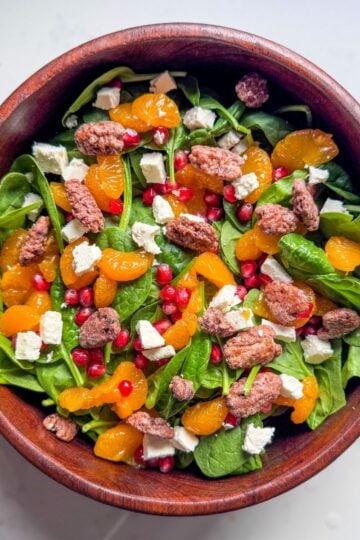 Spinach salad with pomegranate dressing ingredients displayed in a wooden bowl, photographed overhead.