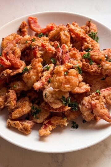 Angled shot of Shrimp Scampi Fritta on a plate with parsley and flaky sea salt, showing the crisp golden coating.