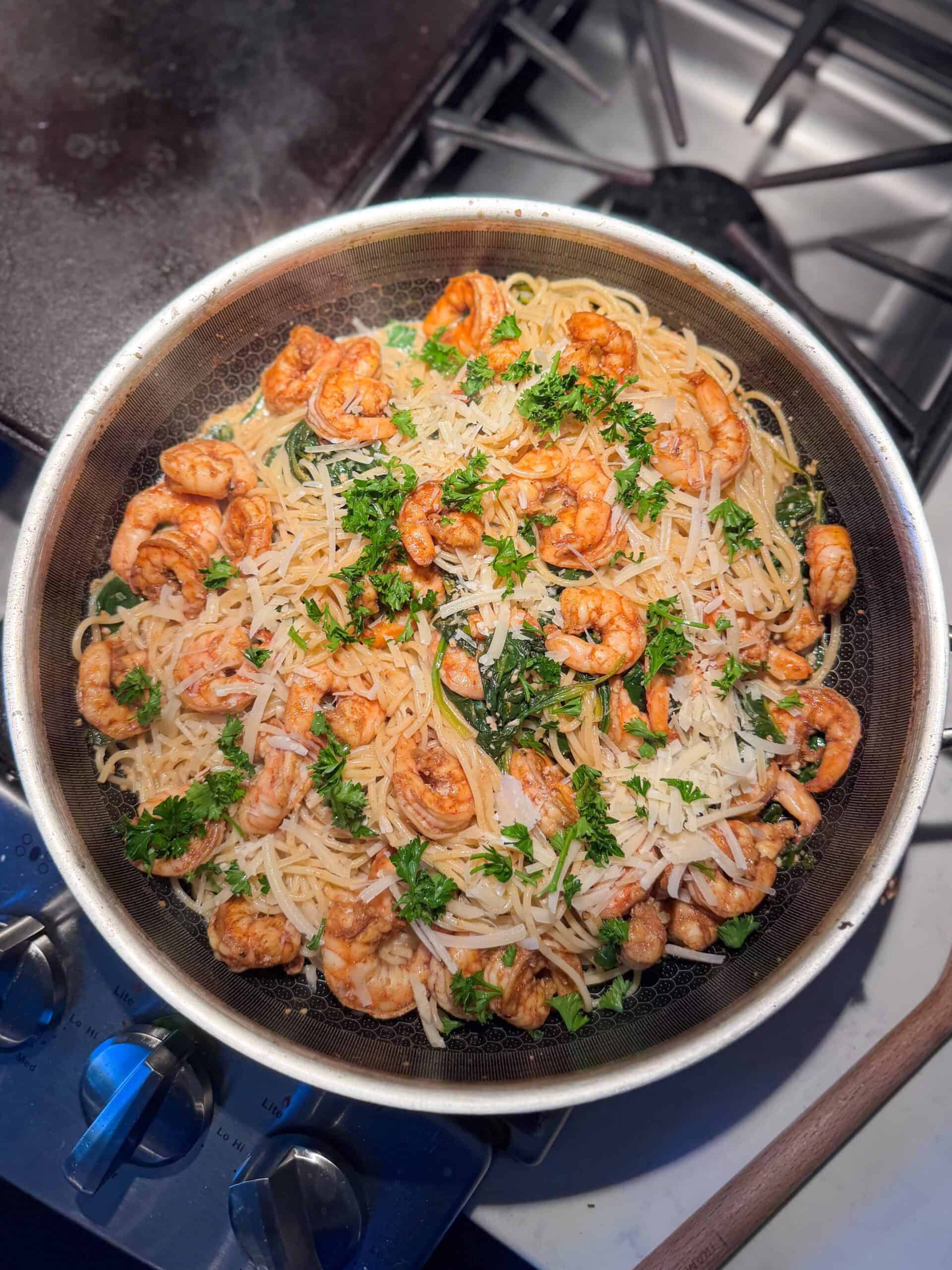 Overhead view of shrimp with spinach and pasta in a skillet with creamy garlic Parmesan sauce.