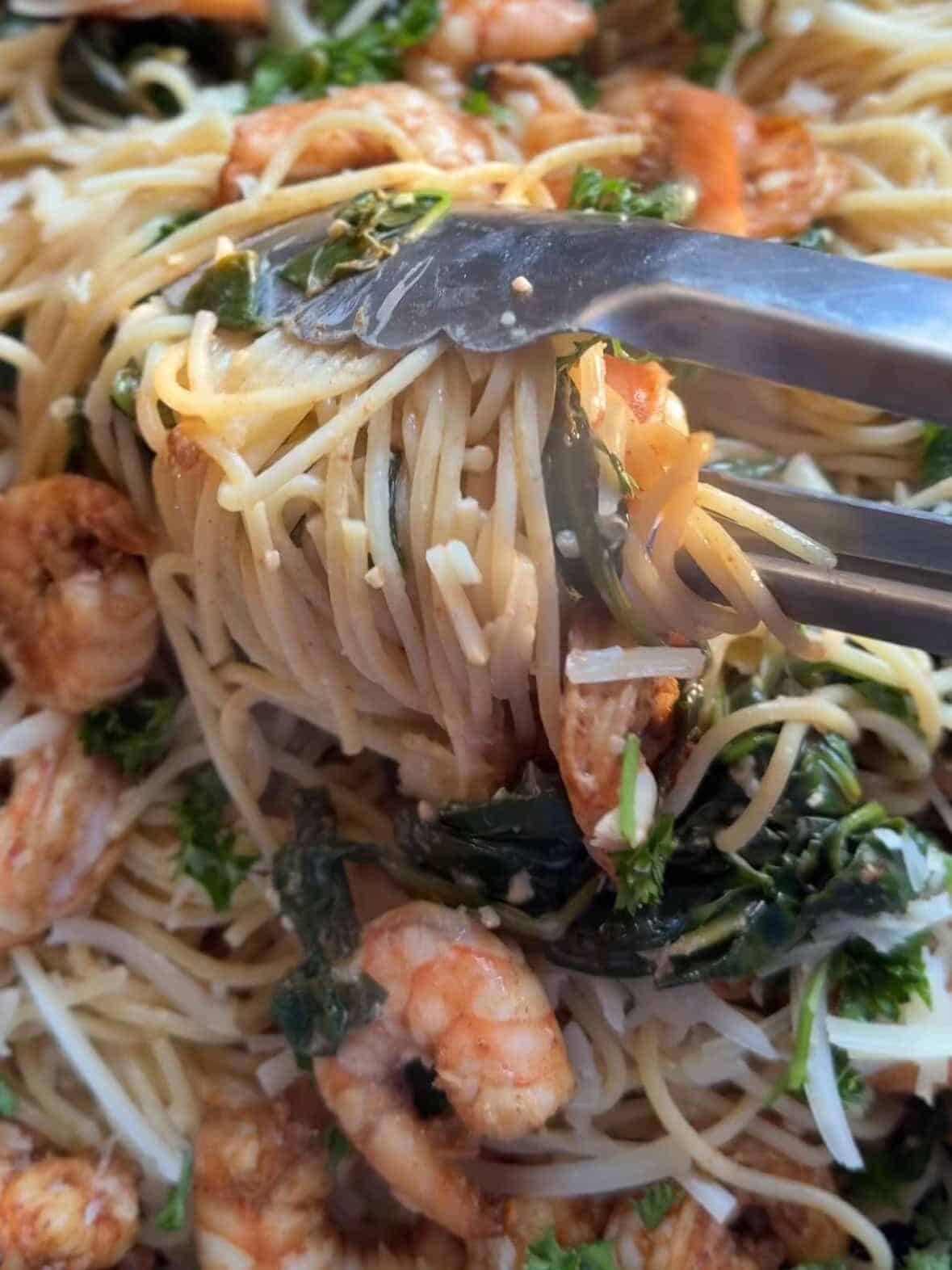 Cooked angel hair pasta tossed with cream, Parmesan, spinach, and shrimp in a skillet.