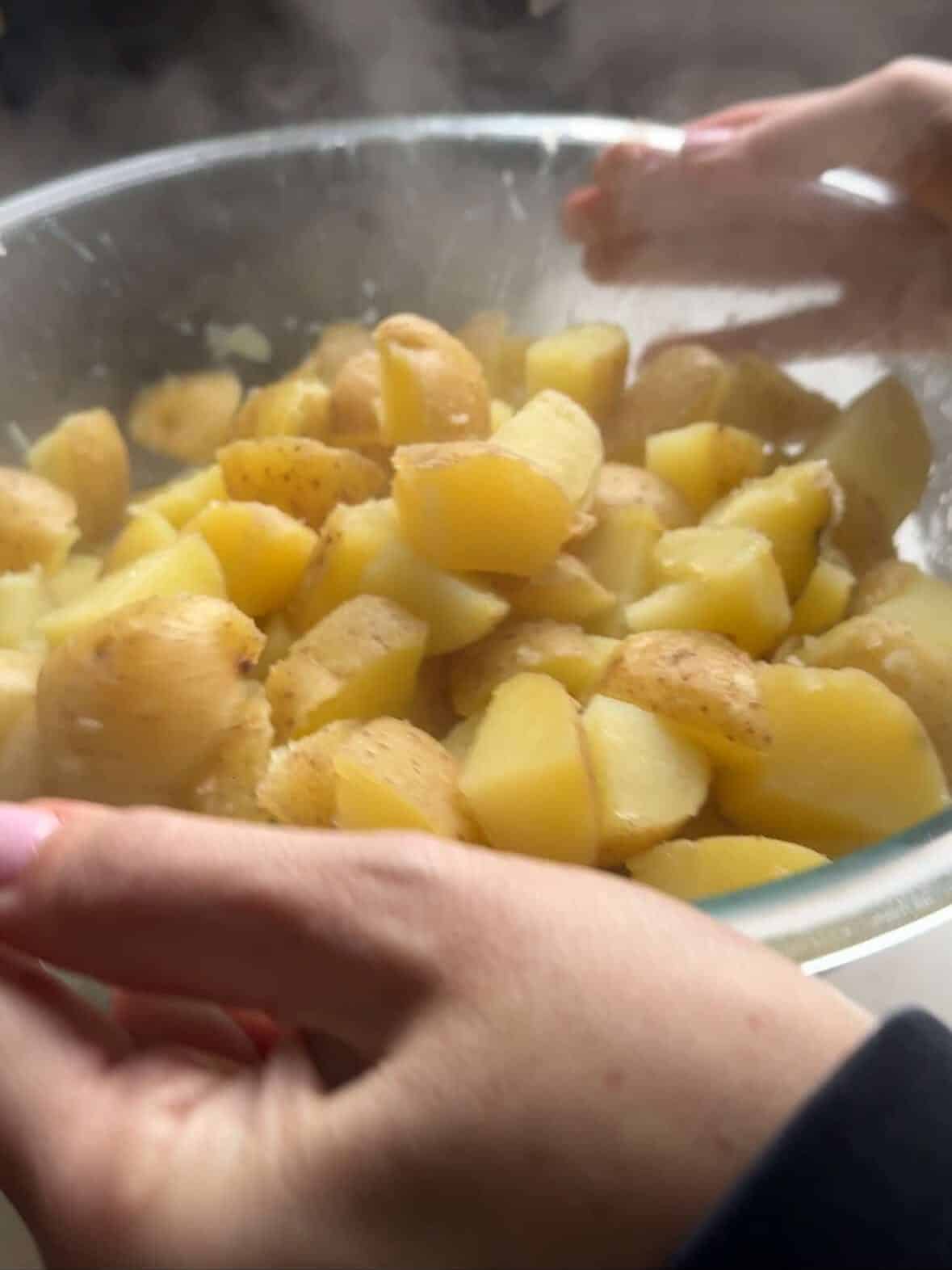 Boiled potatoes being shaken in a glass dish to rough the edges for extra crispiness.