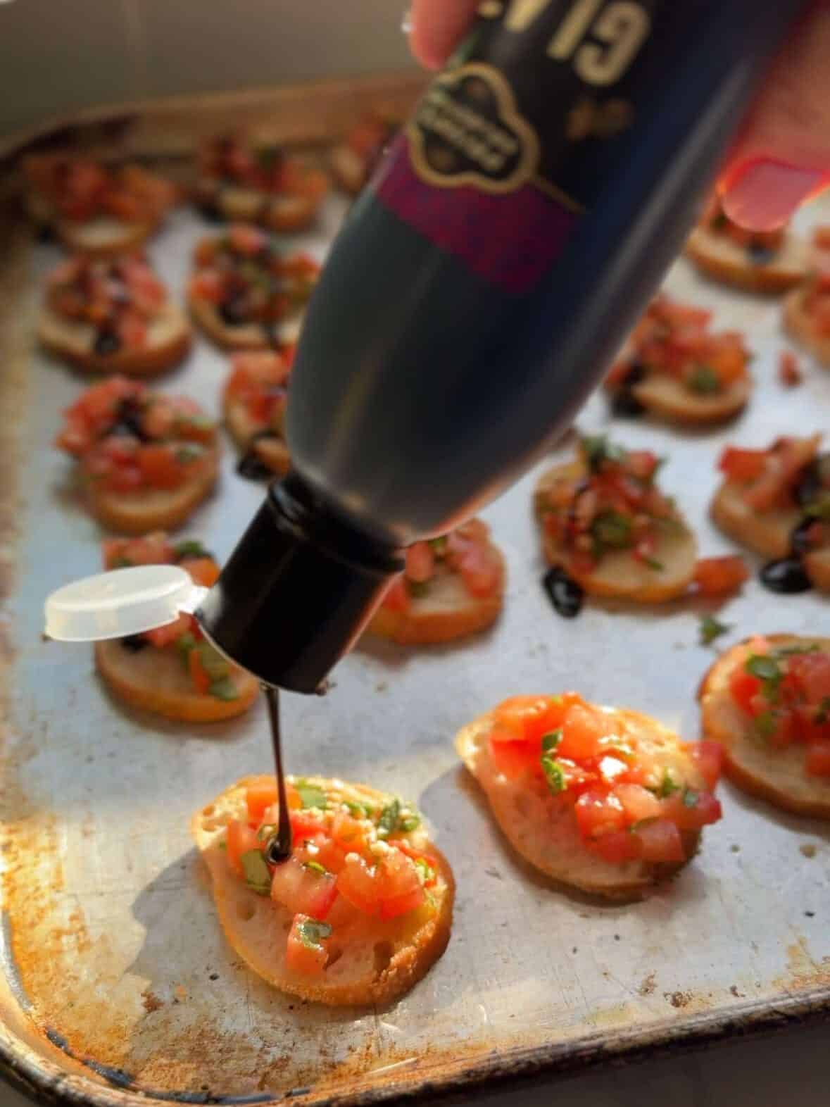 Drizzling balsamic glaze over tomato bruschetta crostini.