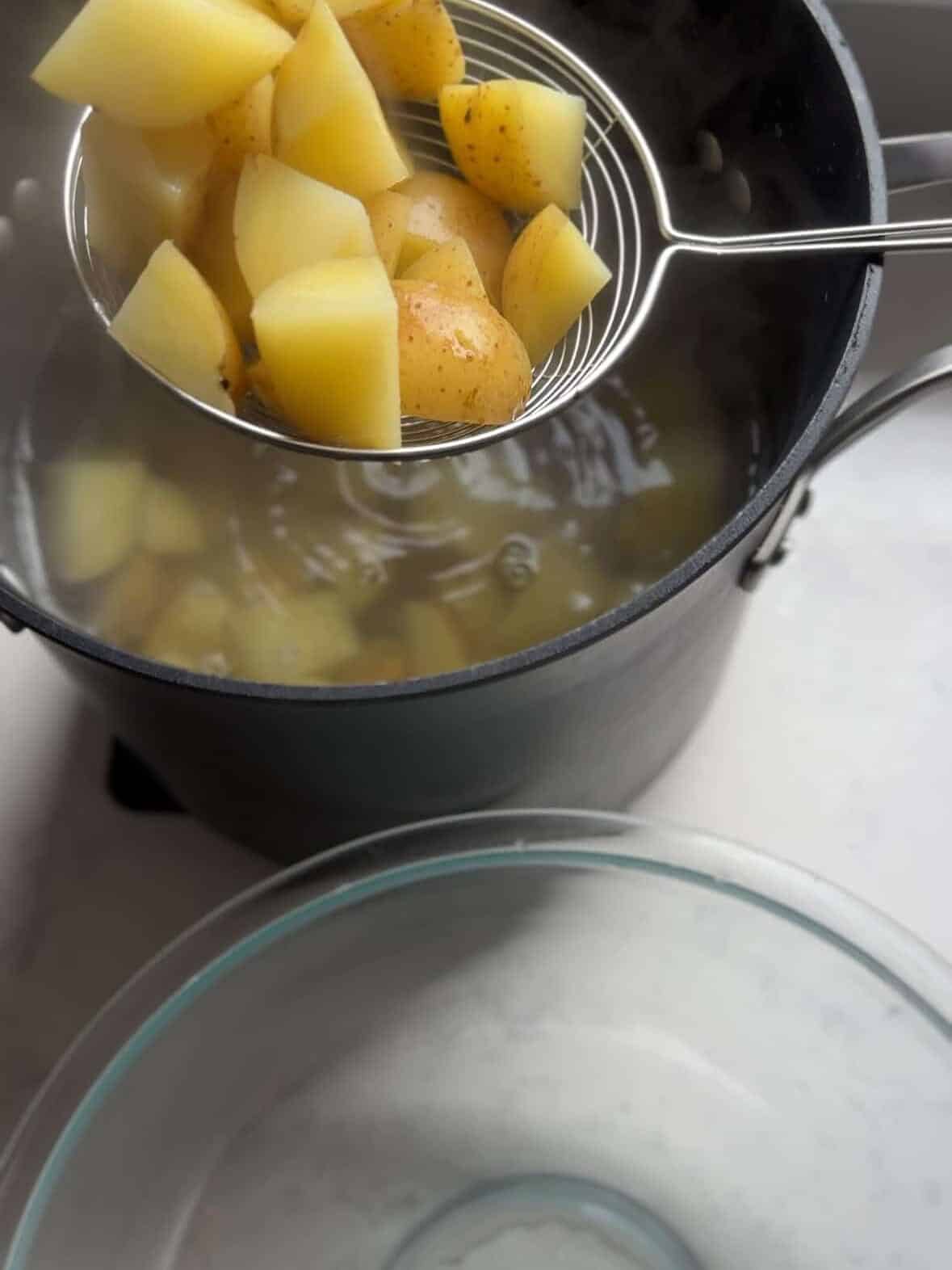 Quartered yellow potatoes simmering in boiling water to begin the crispy roasted potato method.