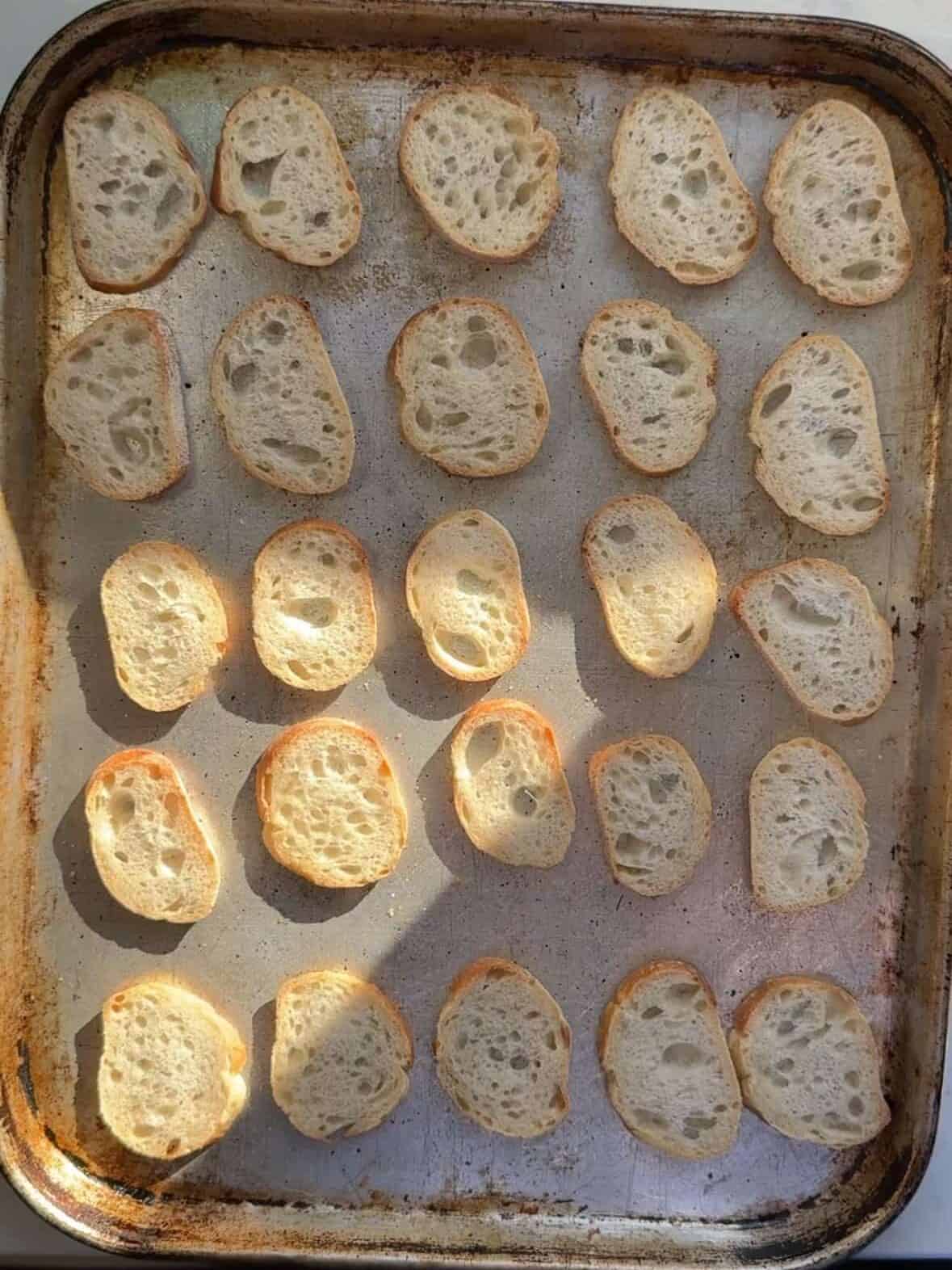 Crisp toasted crostini slices fresh from the oven on a baking sheet.
