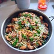 Angle view of shrimp with spinach and pasta in a skillet, with a candle and plant blurred in the background.