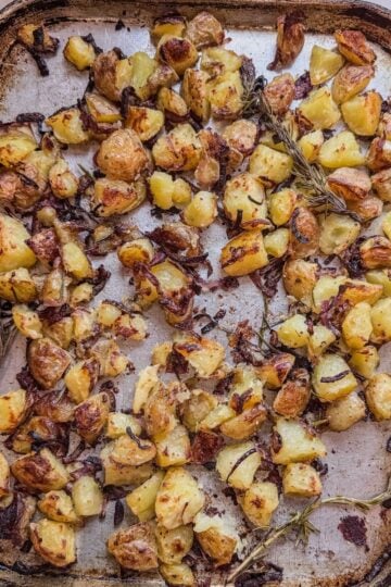 Roasted potatoes on sheet pan showing browning, onions, and rosemary sprigs.