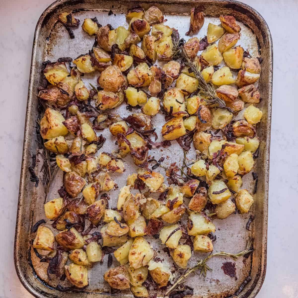 Roasted potatoes on sheet pan showing browning, onions, and rosemary sprigs.