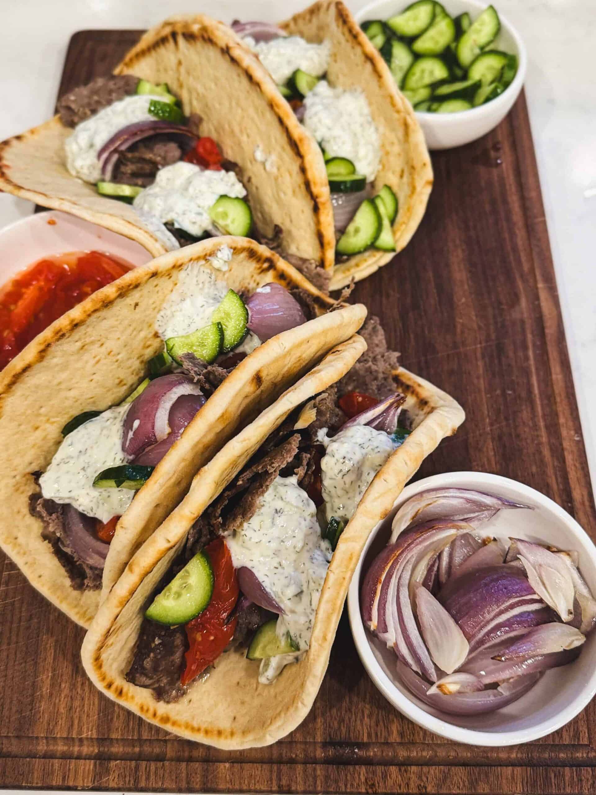 Ground beef gyro sandwiches with tzatziki on a wooden cutting board at an angle