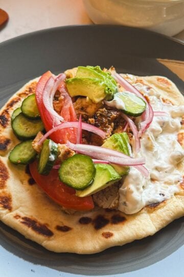 Chicken gyro sandwich made with loaf pan chicken gyro meat, homemade flatbread, tzatziki sauce, pickled cucumbers, red onions, tomato, and avocado