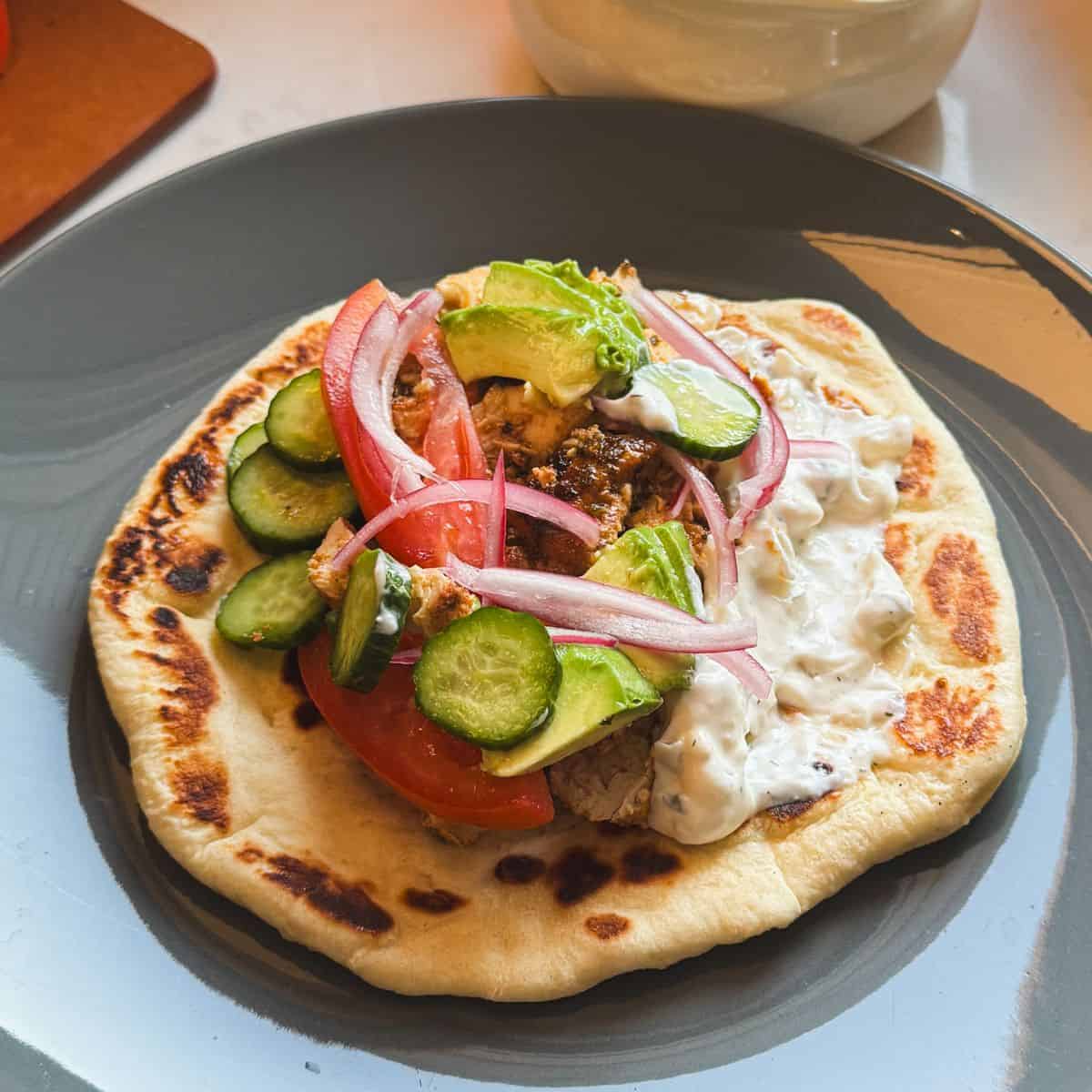 Chicken gyro sandwich made with loaf pan chicken gyro meat, homemade flatbread, tzatziki sauce, pickled cucumbers, red onions, tomato, and avocado
