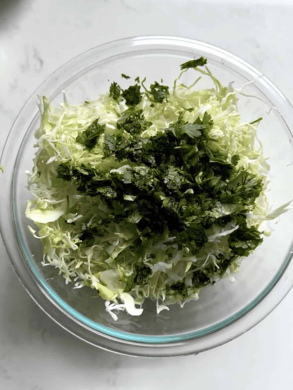Shredded cabbage and fresh cilantro added to a mixing bowl for cilantro lime cabbage slaw