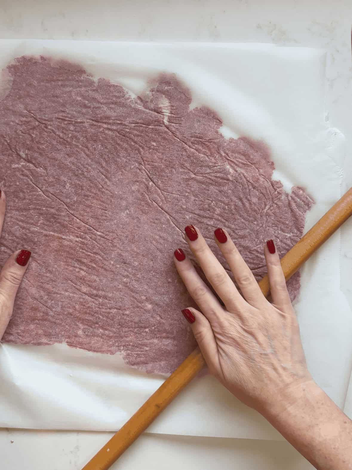 Ground beef gyro meat rolled thin between parchment paper with a rolling pin