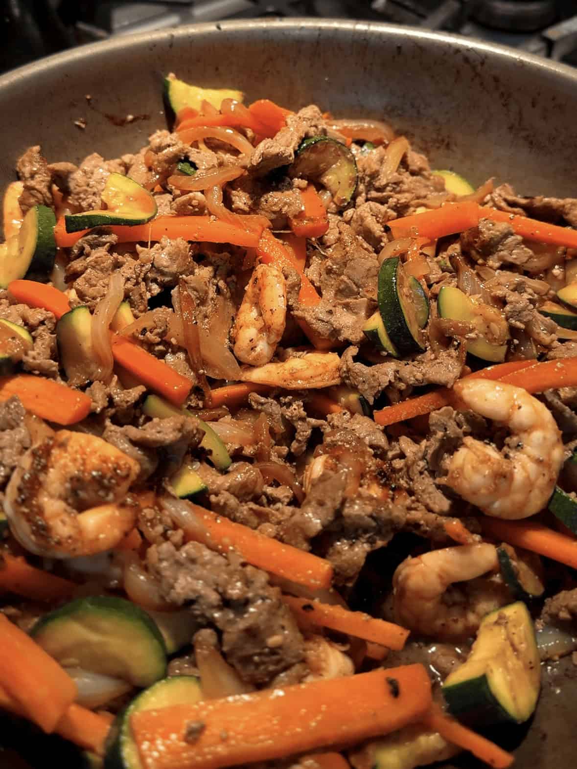 Steak, shrimp, and vegetables being mixed together in a pan for steak and shrimp hibachi bowls cooked using a stir-fry method.
