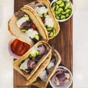 Gyro sandwiches with ground beef gyro meat, tzatziki, tomatoes, onions, and cucumbers on a wooden board