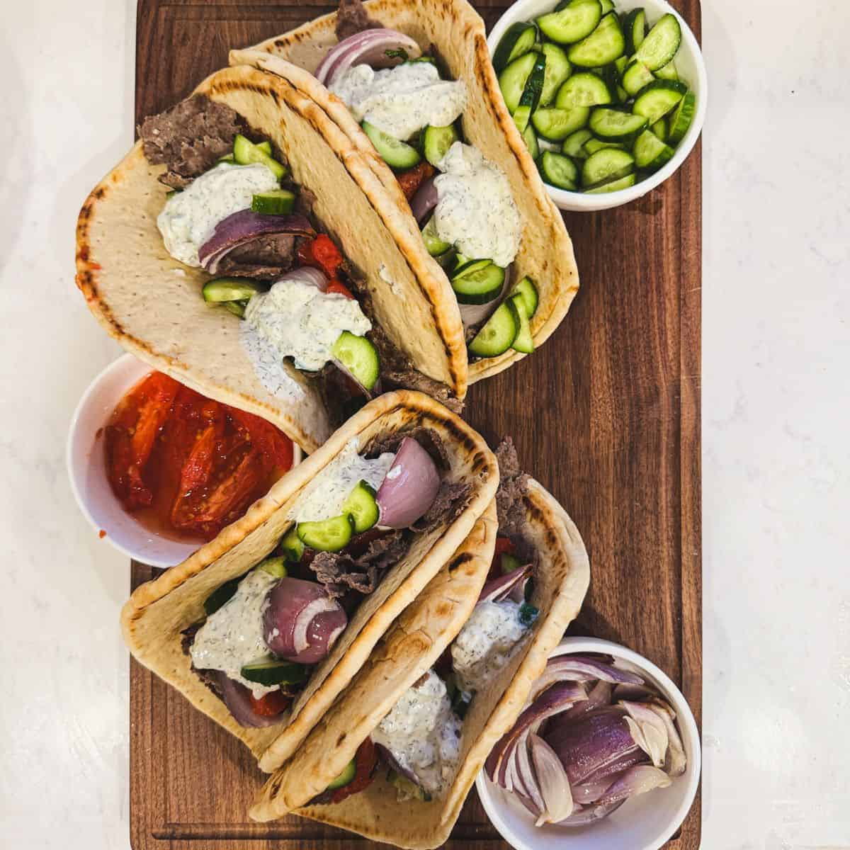 Gyro sandwiches with ground beef gyro meat, tzatziki, tomatoes, onions, and cucumbers on a wooden board