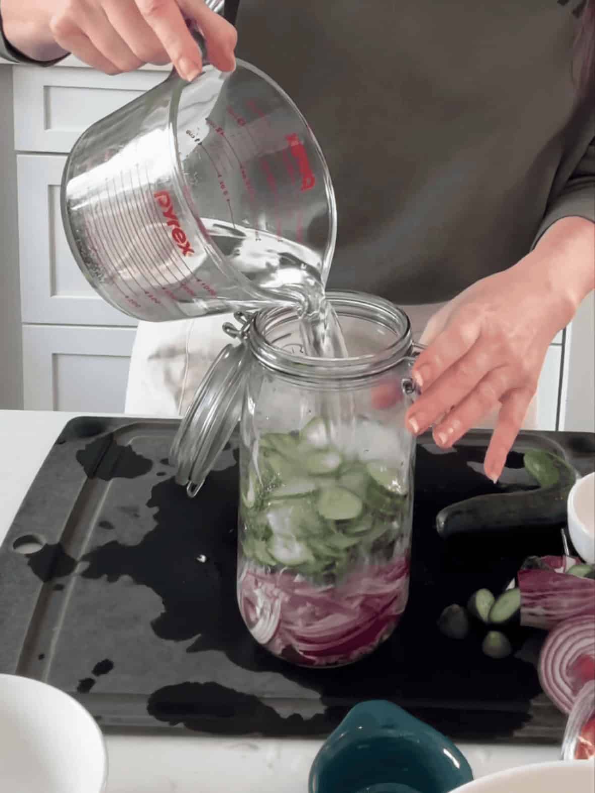 Pouring pickling brine into jar for quick pickled red onions and cucumbers