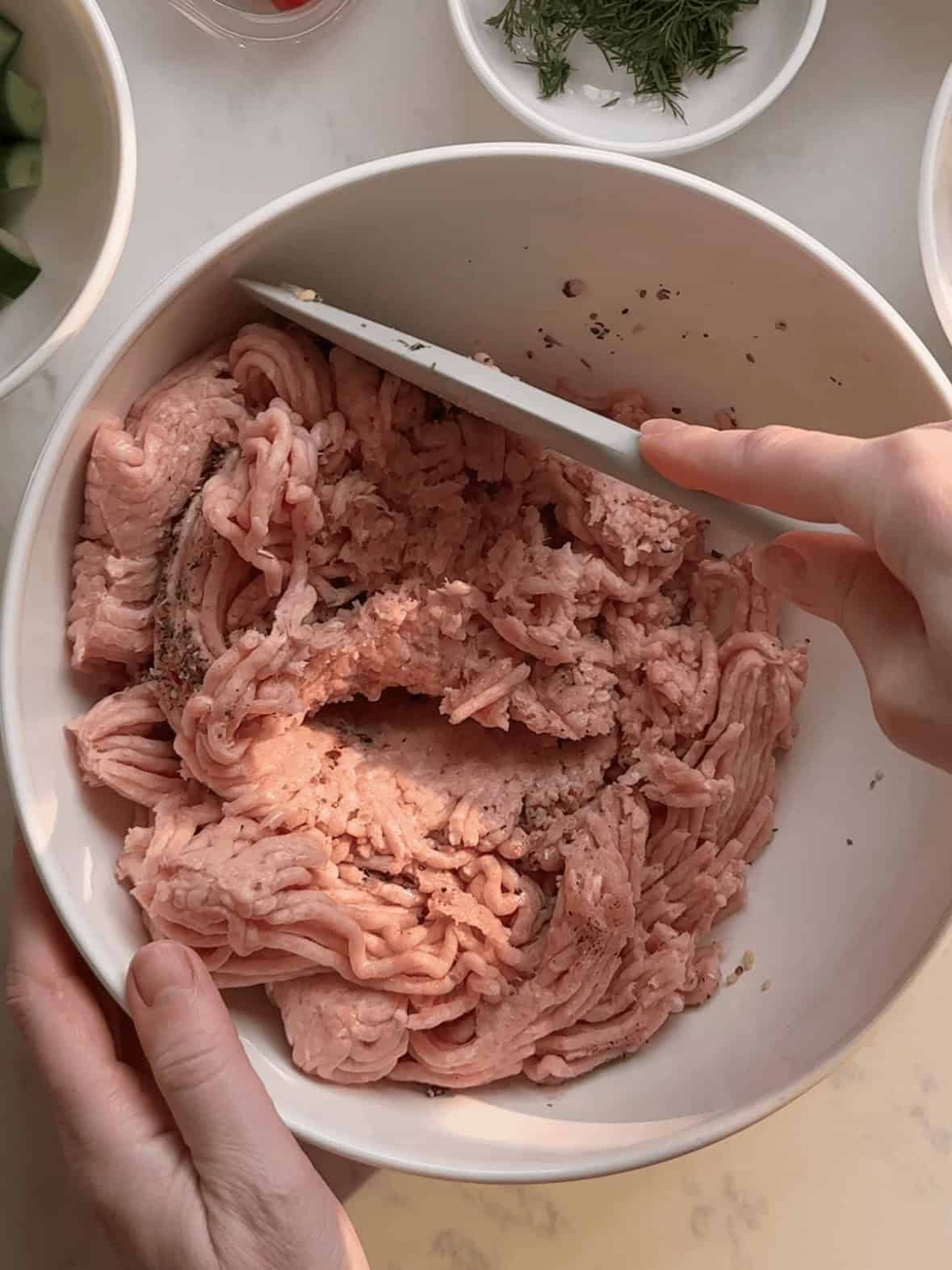 Mixing ground chicken with Greek seasoning and garlic until a paste forms