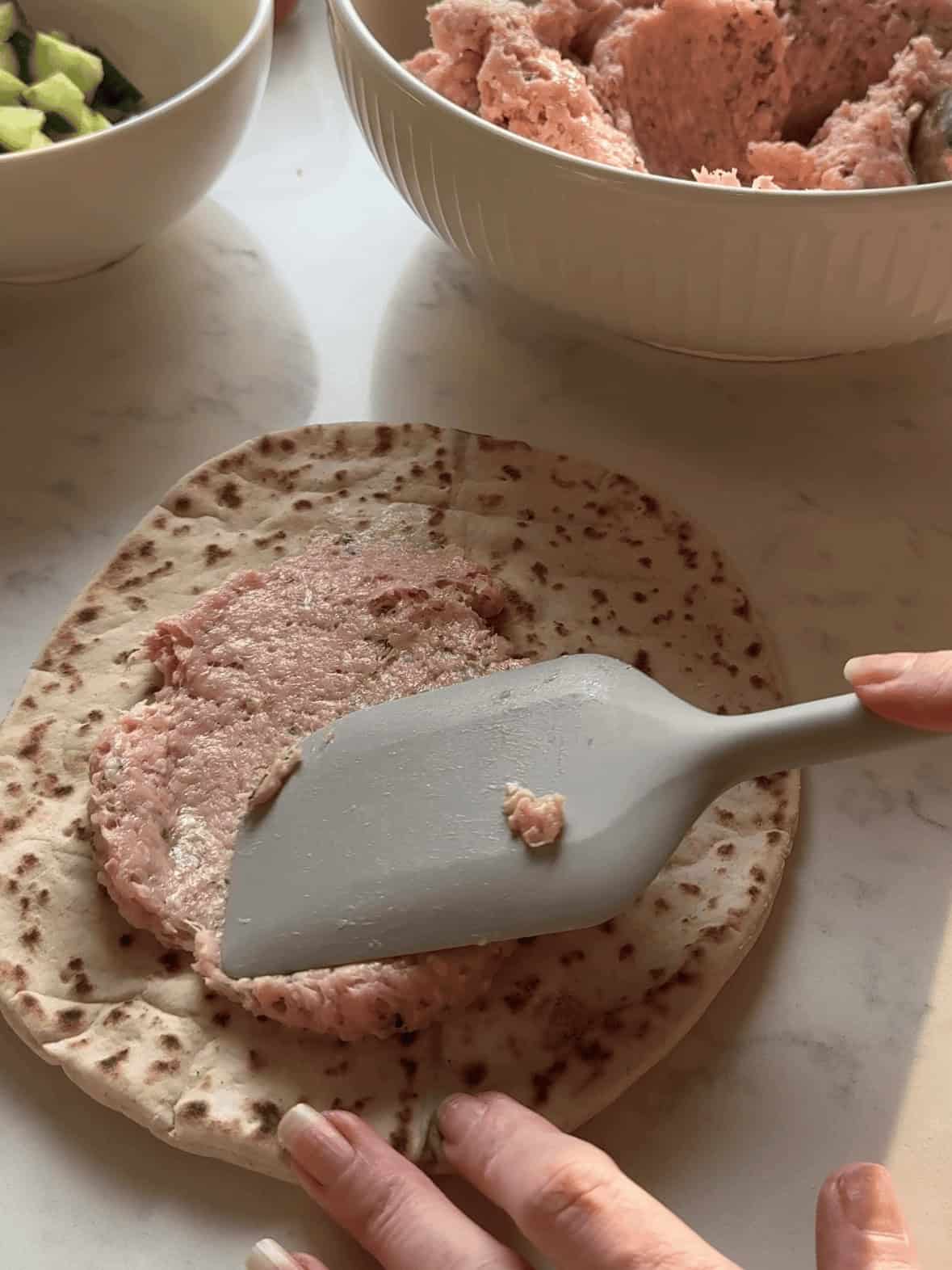 Smashing seasoned ground chicken onto pita bread for Greek smash tacos