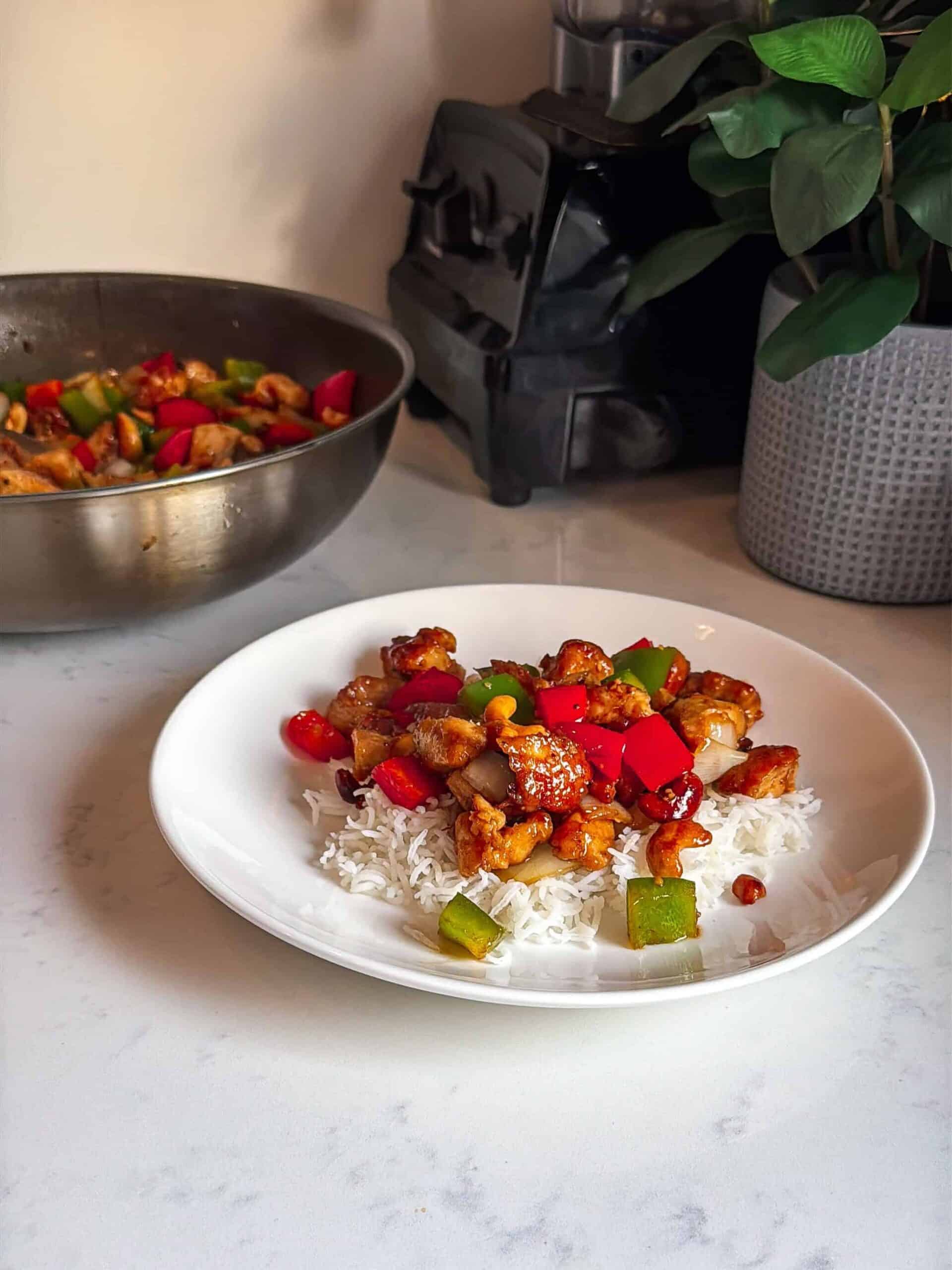 Copycat cashew chicken and peppers served over rice with wok in background