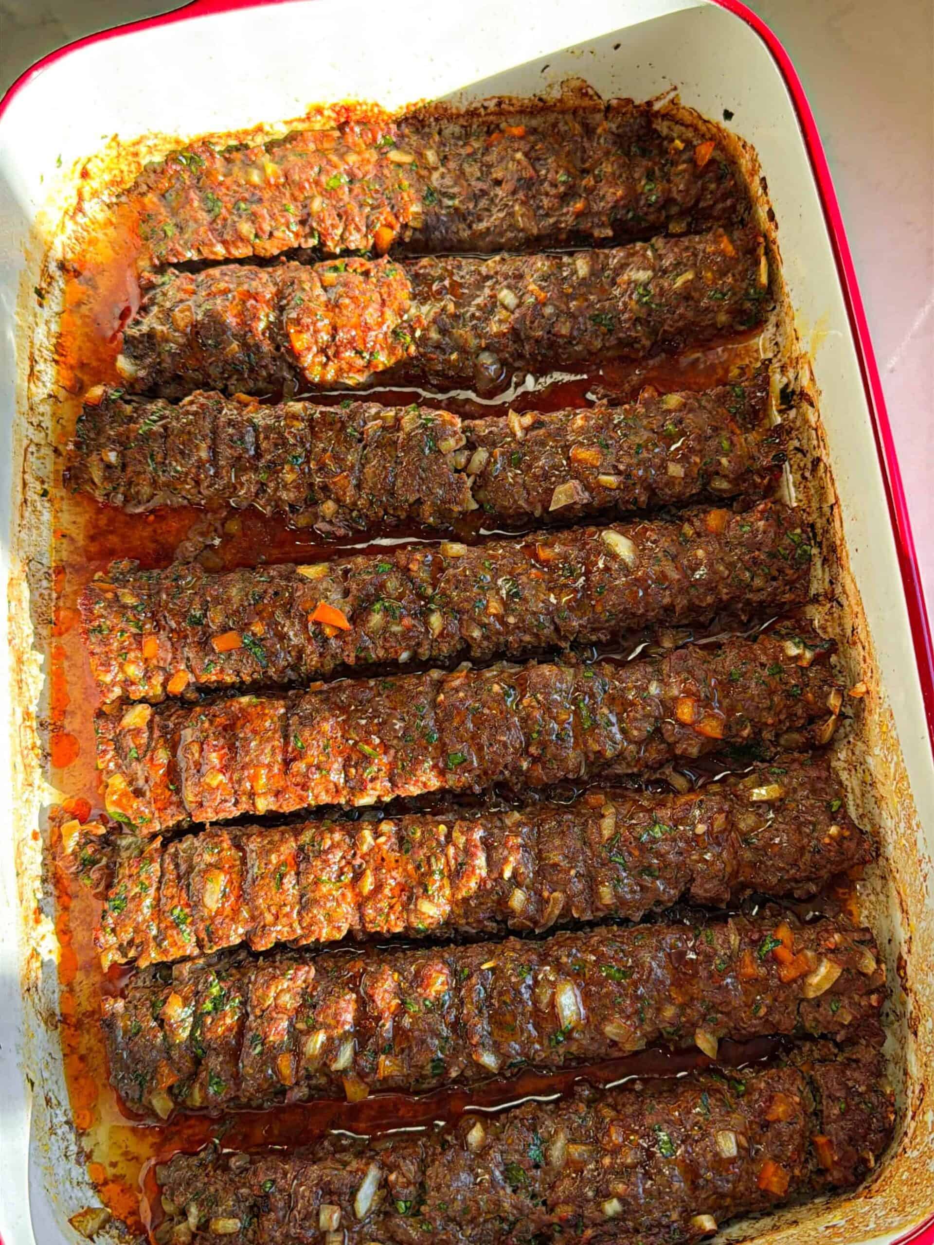 Rows of ground beef kofta shaped in a casserole dish after baking in the oven