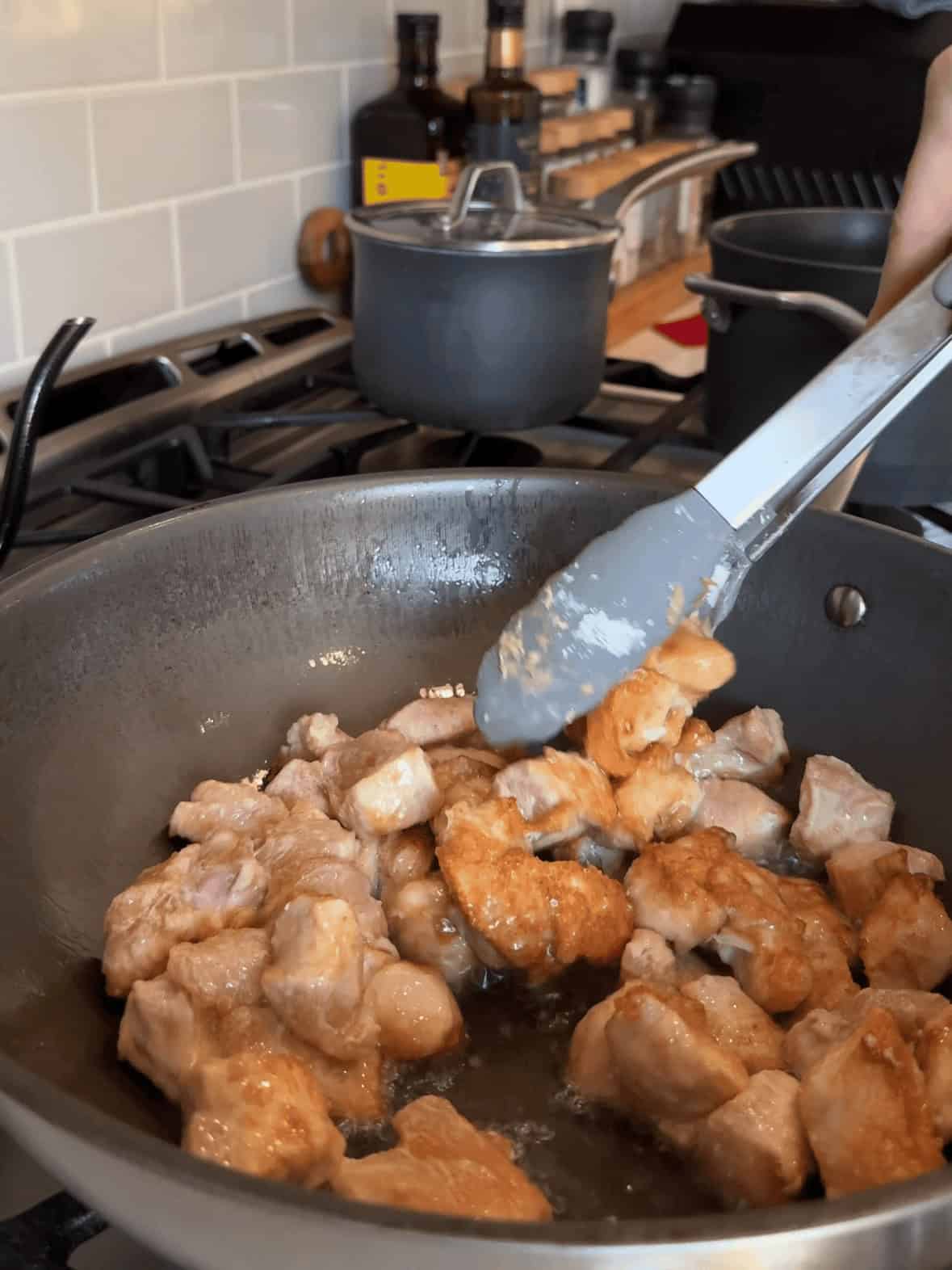 Cubed chicken coated in cornstarch cooking in wok for copycat cashew chicken recipe