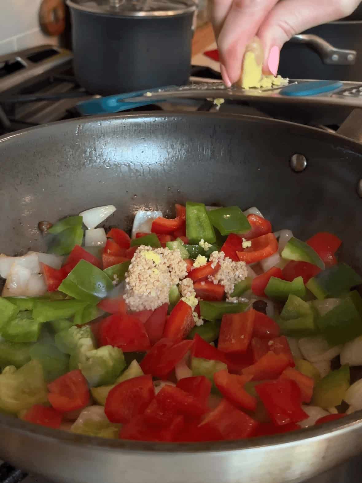 Onions, red and green bell peppers, garlic and ginger sautéing in wok for cashew chicken and peppers recipe