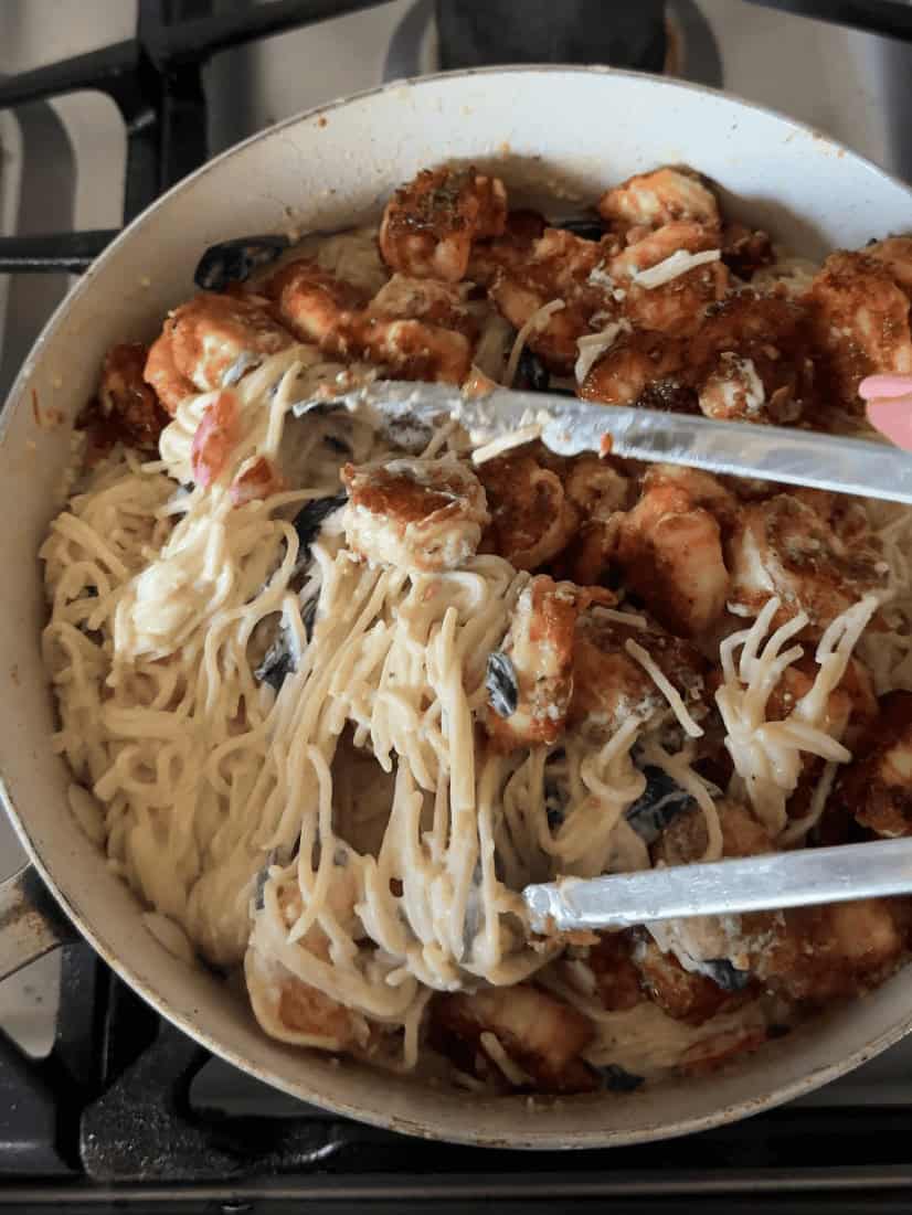 Mixing spaghetti shrimp spinach and roasted red peppers in creamy pasta sauce