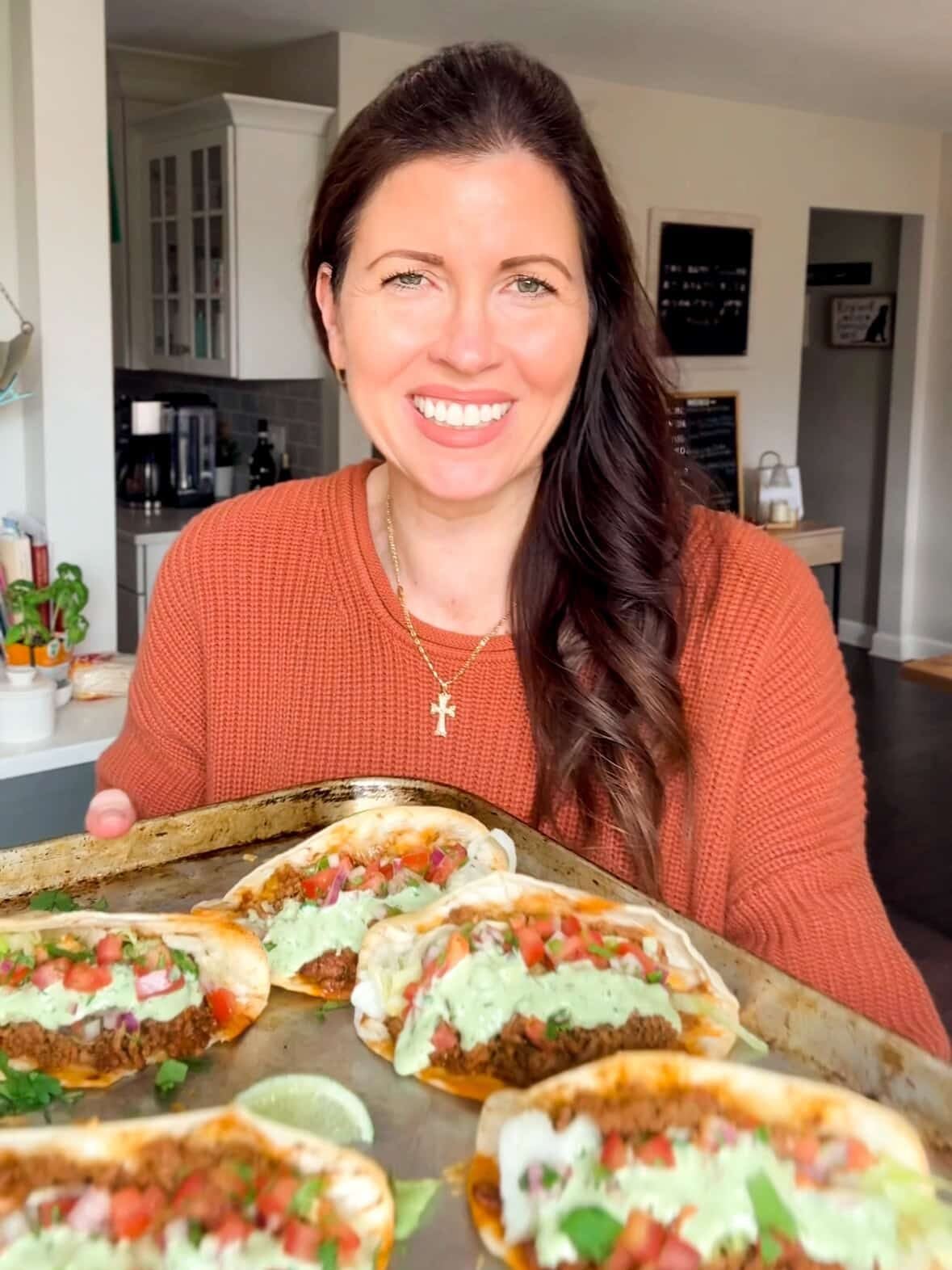 holding sheet pan of crispy oven baked beef tacos with cilantro lime crema