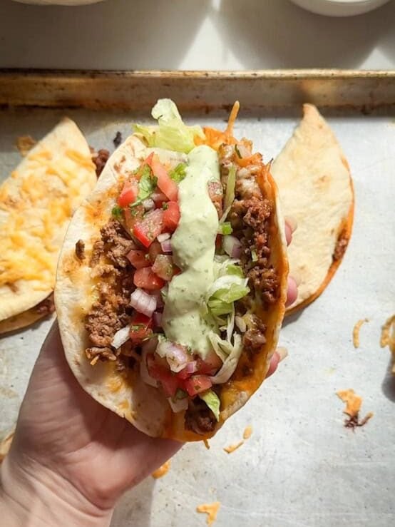 hand holding crispy baked taco with cilantro lime crema and pico de gallo