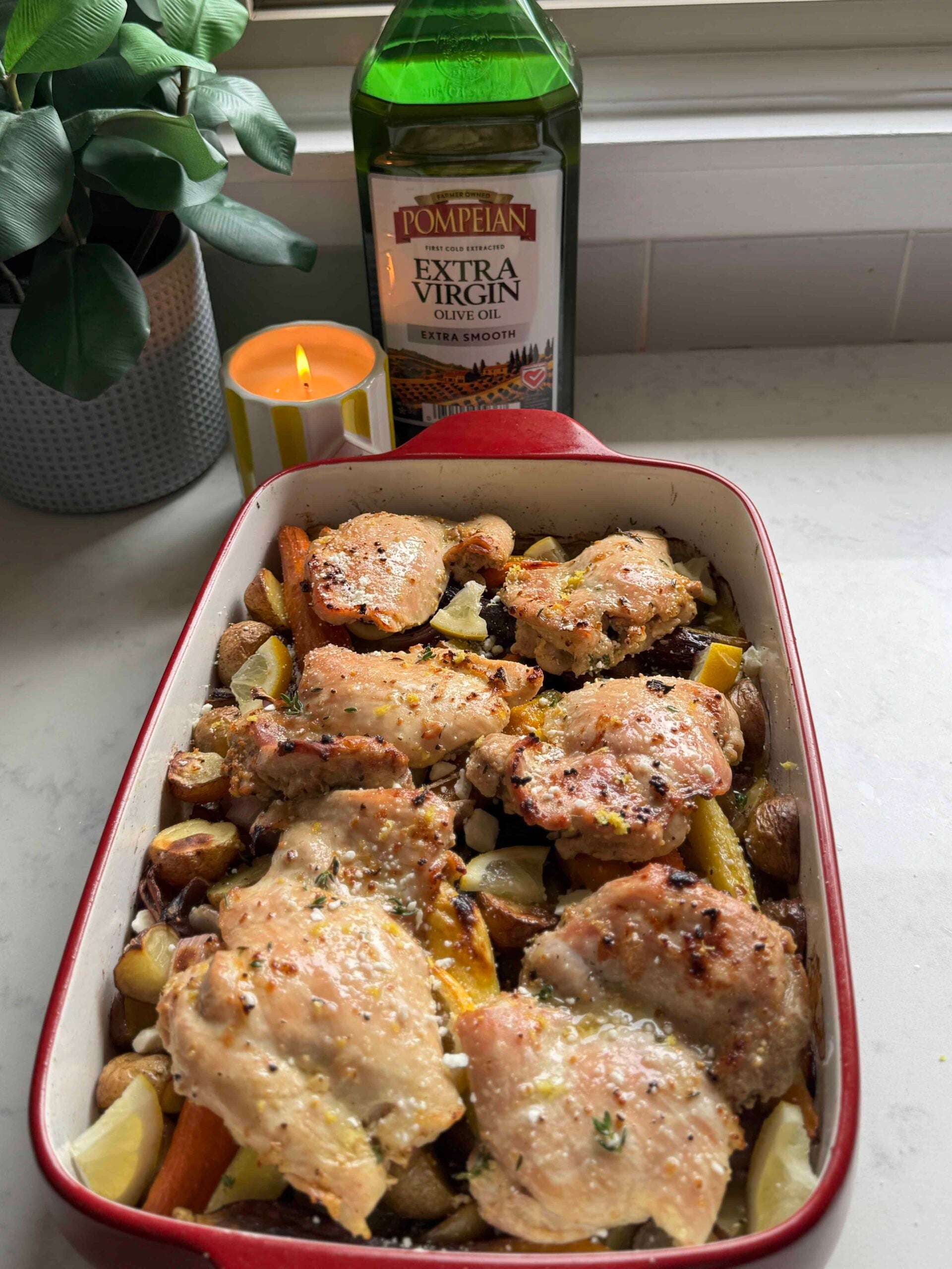 One pan chicken thighs and veggies in a casserole dish with roasted potatoes, carrots, red onion, lemon, and feta at a 45 degree angle
