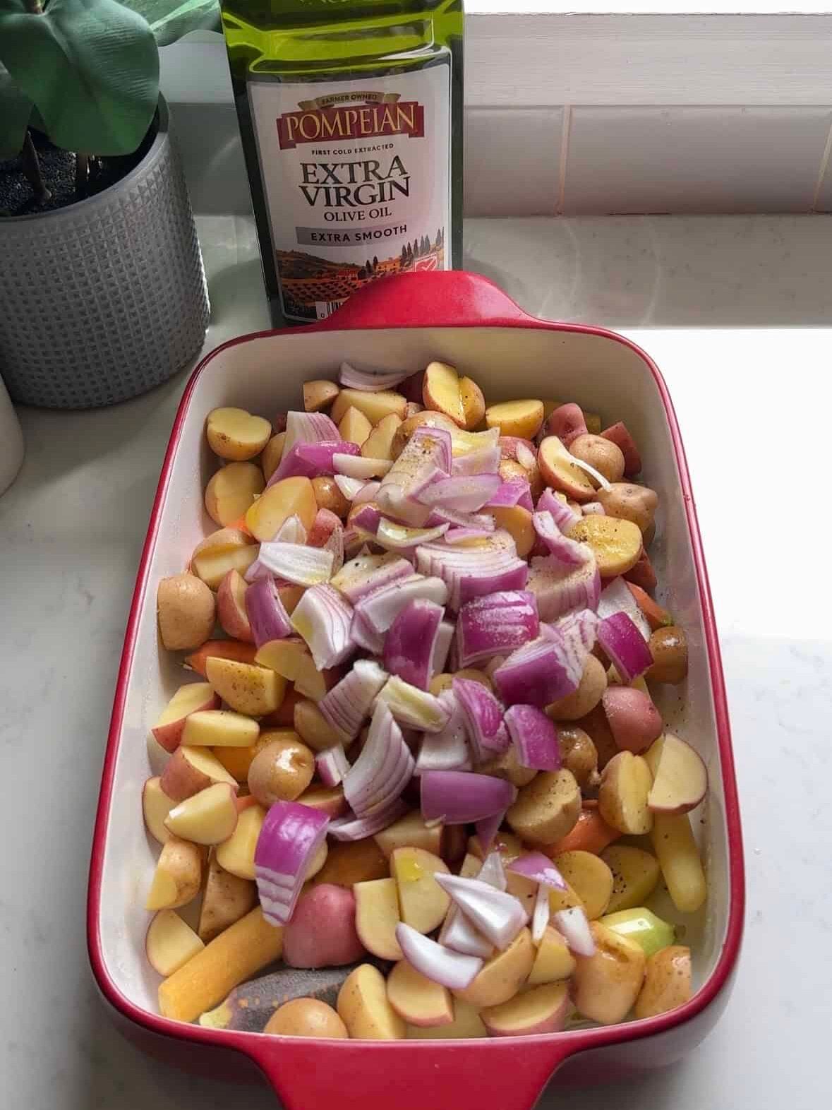 Baby potatoes, rainbow carrots, and red onion tossed with olive oil in a baking dish for one pan chicken thighs and veggies