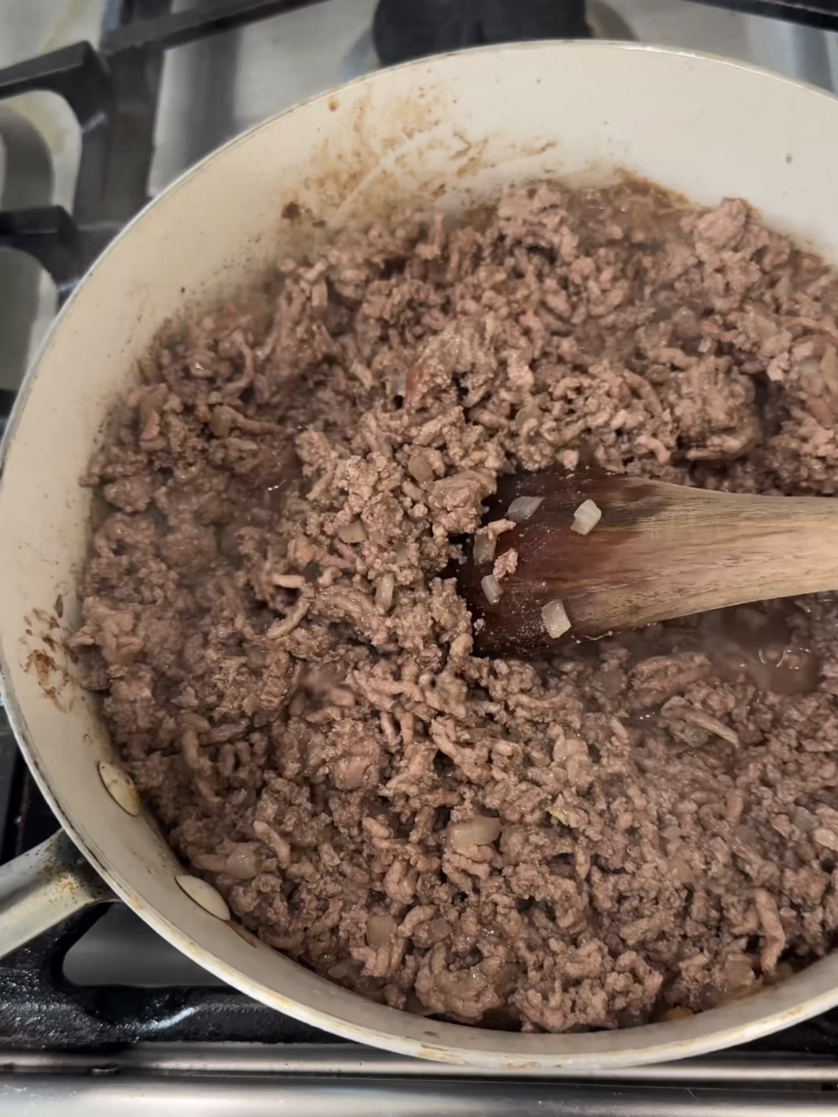 ground beef and diced onions cooking in skillet for crispy oven baked tacos.