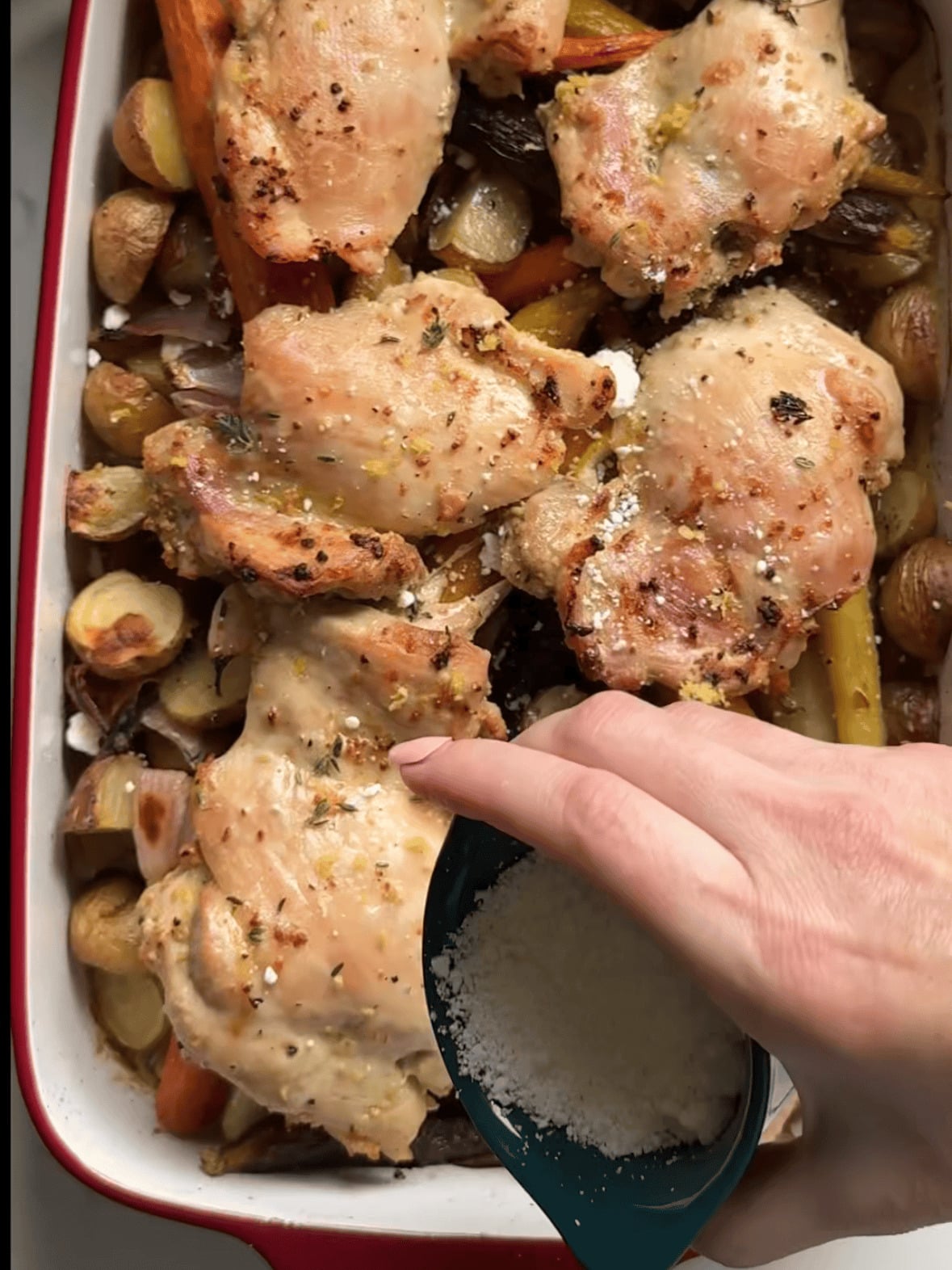Adding feta cheese to baked one pan chicken thighs and veggies with potatoes, carrots, red onion, lemon, and thyme