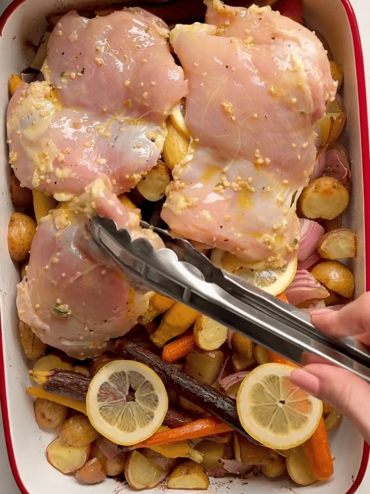 Lemon slices and marinated chicken thighs added over roasted potatoes, carrots, and onions for one pan chicken thighs and veggies